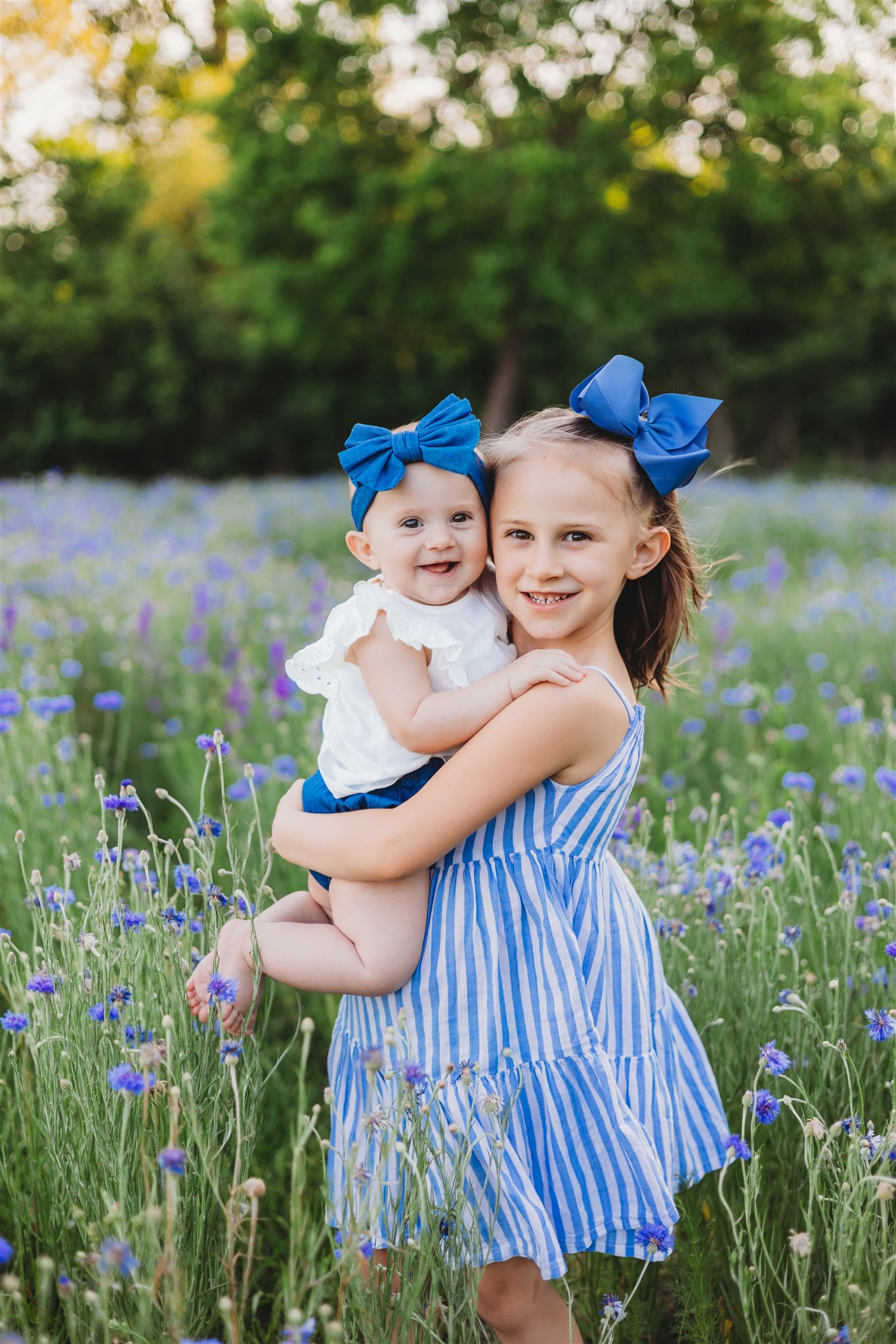 little girl in blue dress holding her sister in a field